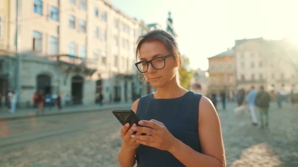 Woman Walking Down an Old Street and Using Smartphone at Sunset. Slow Motion alt