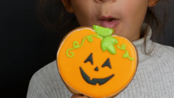 Halloween. Little girl bites pumpkin-shaped gingerbread. Halloween sweets and treats.