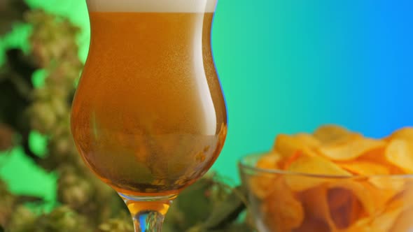Pouring beer in tulip glass on table with potato chips and hop flowers. 2x slowmotion 24fps