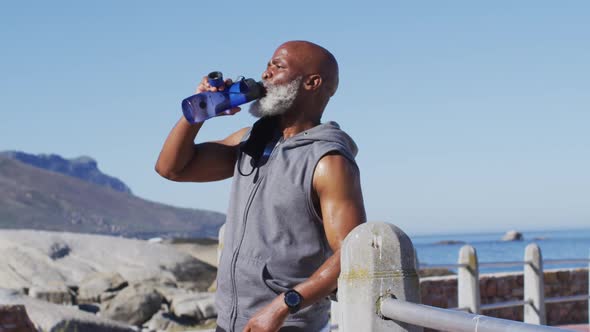 Senior african american man exercising drinking water on rocks by the sea alt