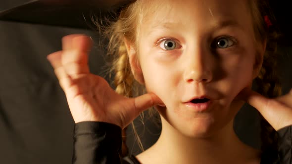 Little pretty girl witch in black wizard hat says Boo laughs Smiling child dressed in ghost costume alt