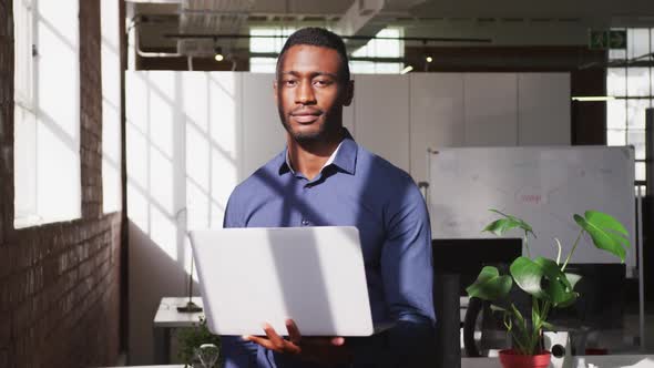 African american businessman holding laptop looking ahead shifting gaze to camera and smiling alt