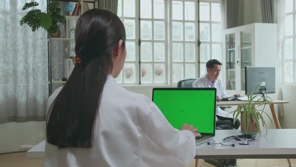 Asian Woman Doctor Is Using Laptop Computer With Mock Up Green Screen Display In Workplace alt