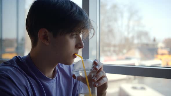 A Handsome Young Man Drinks a Healthy Orange Smoothie in a Cafe