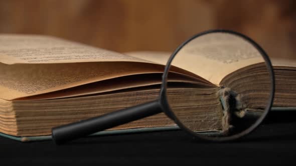 Pages of an Old Book are Turning Next to a Magnifying Glass alt