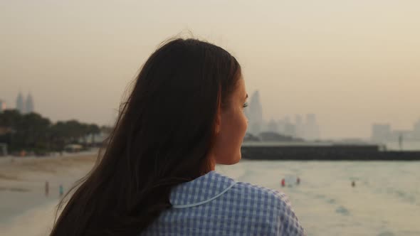 Woman Looking at Sand Beach and City Skyline Across the Water alt