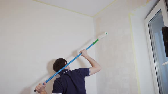 Caucasian Man Paints a Wall with a Roller Over His Head with His Hands alt