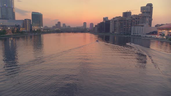 An Aerial View of a Boat That Floats on a River in the City Centre at Sunset alt