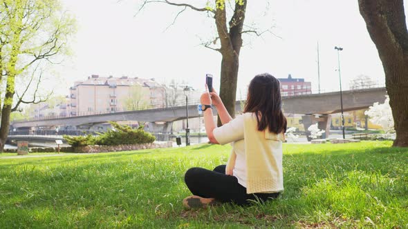 Back view of Asian Straight hair woman sitting on the ground and taking a photo of river alt