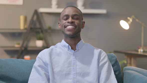 Portrait of African Man Showing Yes Sign While Sitting on Sofa alt