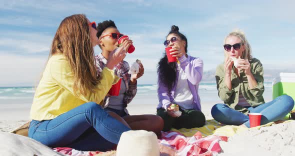 Happy group of diverse female friends having fun, having picnic at the beach alt