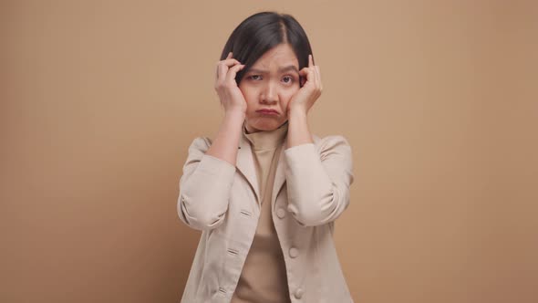 Asian business woman feel confused standing and looking at camera isolated over beige background.