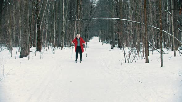 A Young Blonde Woman in Red Down Jacket Skiing with an Effort in the Woods alt