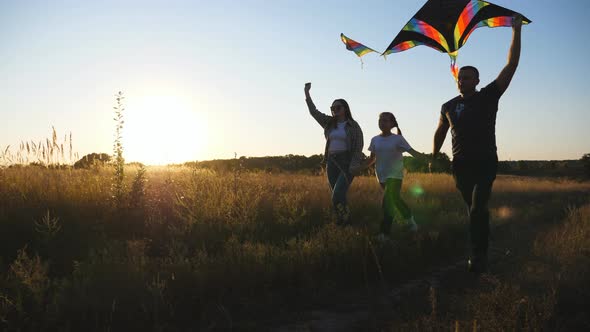 Mother and Father with Little Daughter Jogging with Rainbow Kites on Rural Path at Sunset alt