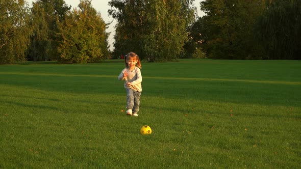 Girl Plays to Football Outdoors in Summer Park