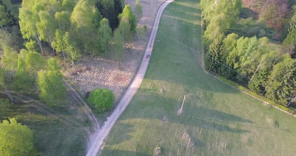 Aerial drone view of a country dirt road with green trees and hills. alt