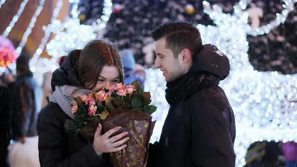 A Man Makes a Gift To a Woman on the Street Decorated with Lights alt