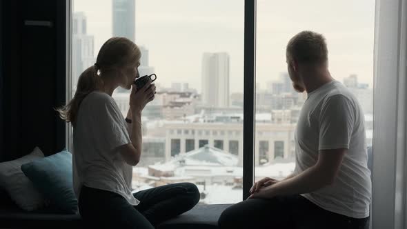 couple communicates sitting on the windowsill by the window overlooking the city