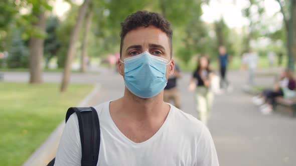 A Young Handsome Man Stands in the Park in the Alley Wearing a Protective Mask During the alt