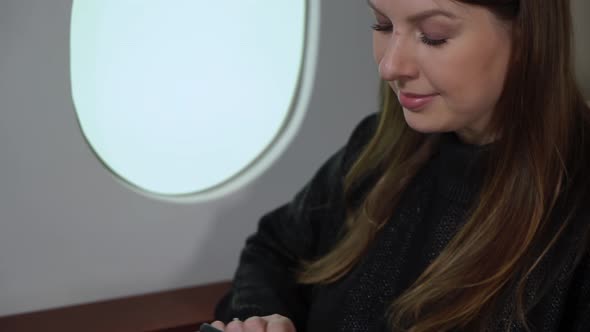 Woman in Airplane with Mobile Phone Using Smartphone in First Business Class or Private Jet Flight alt