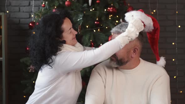 Woman Putting Santa Hat on Her Handsome Husband at Christmas alt