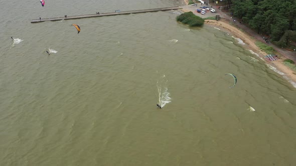 AERIAL: Follow Shot of Isolated Kiteboarder Who Jumps Over Stone Pier on a Cloudy Day alt