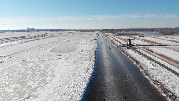 People ice skating on frozen Dutch canal in windmill polder land, winter scene alt