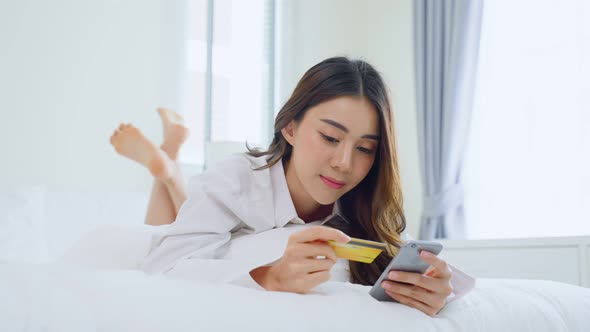 Happy casual beautiful female lying down in bedroom enjoy use mobile phone and chat online on bed alt