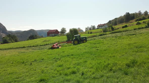 A Farmer Driving A Green Tractor Pulling A Mower Through A Lush Grassy Field, Cutting Grass For Sila alt