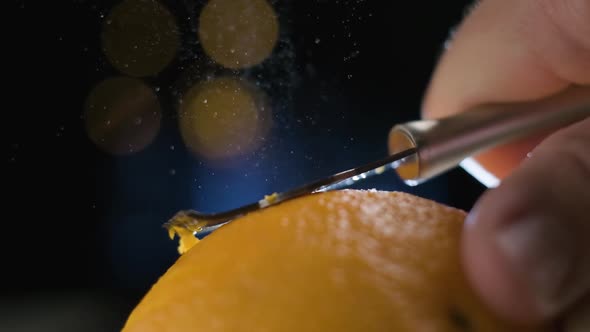 Slow motion macro shot Orange peel Spraying Citrus Oil Partlicles on Blurred Lights Background alt