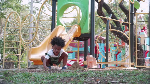 A cute African American boy playing sand in a sandbox area in playground