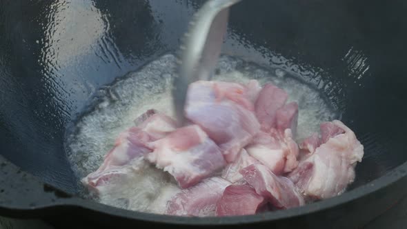 Cooking Process, Frying Pork Meat In Large Cauldron On Open Fire alt