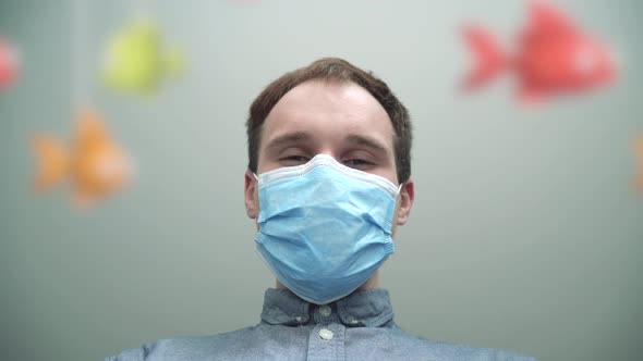 The young father in a medical mask looks at his baby laying in a baby crib