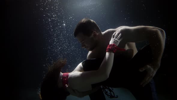 Dancing Pair Inside Water of Swimming Pool Man Is Hugging Slender Sexy Woman and Looking at Camera alt