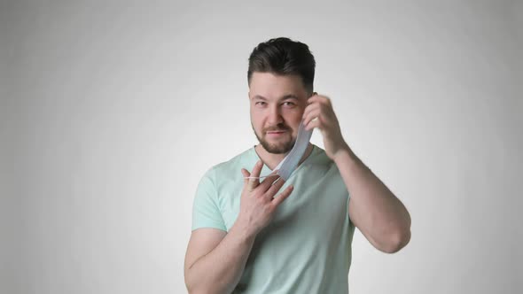 Young Bearded Man in Green Tshirt Putting on Mask on Face on Grey Background alt