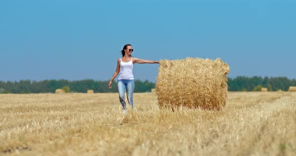 Beautiful Girl is Walking Along a Golden Mown Field There are Haystacks alt