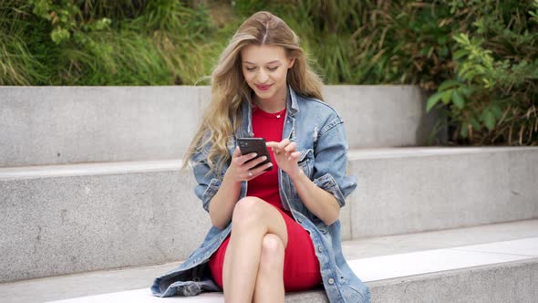 Young Woman with Smartphone Sitting on Street