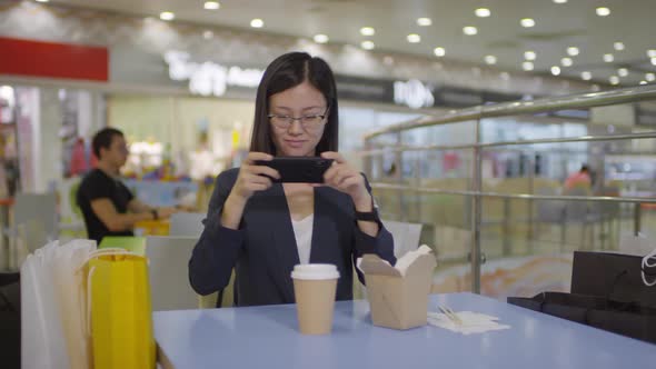 Delighted Asian Woman Taking Photos on Smartphone in Shopping Mall alt