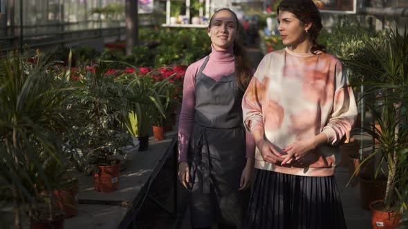 Young Smiling Female Florist Walking with Her Boss and Showing Her Different Plants Explaining alt