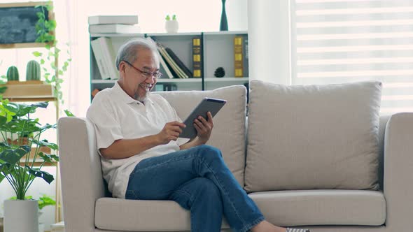 Happiness elderly asian man sitting on sofa and using computer tablet VDO Conference online alt