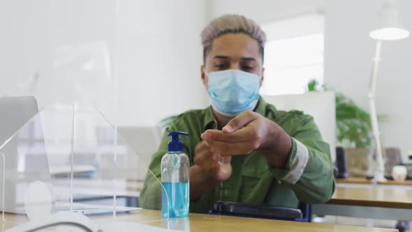 Man wearing face mask sanitizing his hands at office alt