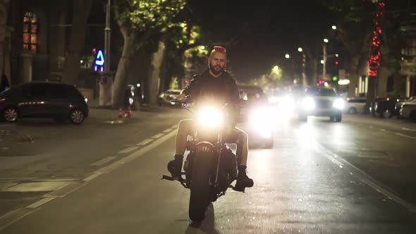 Front View of a Brutal Motorcyclist Drives a Bike in the City with Bright Headlight at Night alt