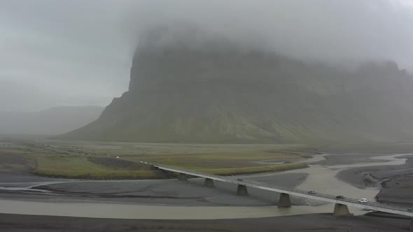 Aerial shot of a one way bridge with a mountain in the horizon on a foggy day in Iceland. alt