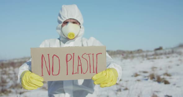 Man Wore in Protective Suit Holds No Plastic Sign on Abandoned Place in Winter alt