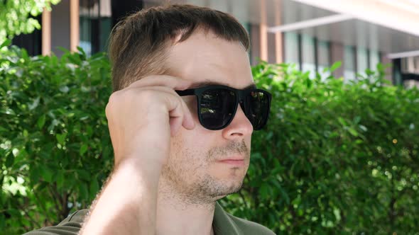 Man Looking From Under Black Sunglasses Showing Bloodshot Eye with Inflammation alt