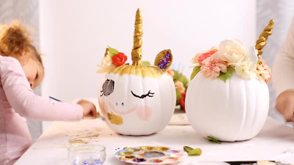 Little girl and her mother painting face of a unicorns on her craft pumpkin for Halloween. alt