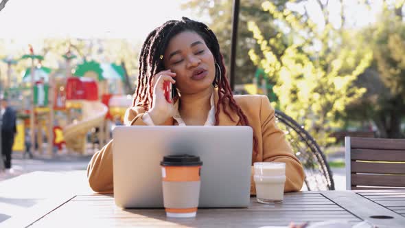 Young African American Woman Sitting in Outdoor Cafe and Using Laptop