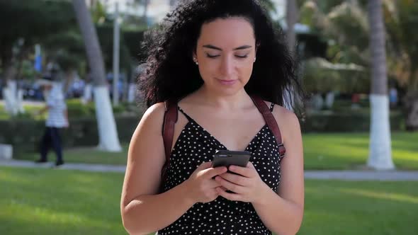 Young Woman or Girl Is Texting Messages on the Phone on a Sunny Day on a Background of Palm Trees alt