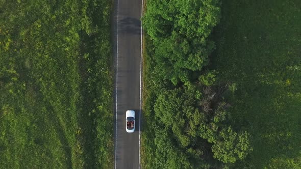 Aerial Shot of White Convertible Car Riding Through Empty Rural Road alt