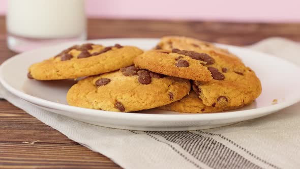 Female Hand Taking Chocolate Chip Cookie From a Plate on Wooden Table Close Up